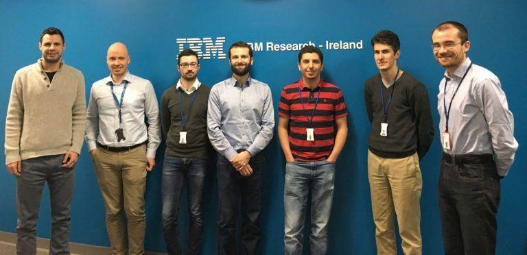 Photograph of seven scientists standing against a blue wall with the words IBM Research - Ireland and the IBM logo on it.