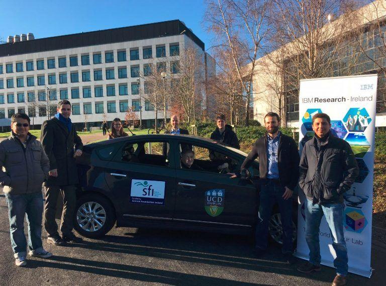 Photograph of 8 scientists around a car in front of the IBM Research Ireland lab building.